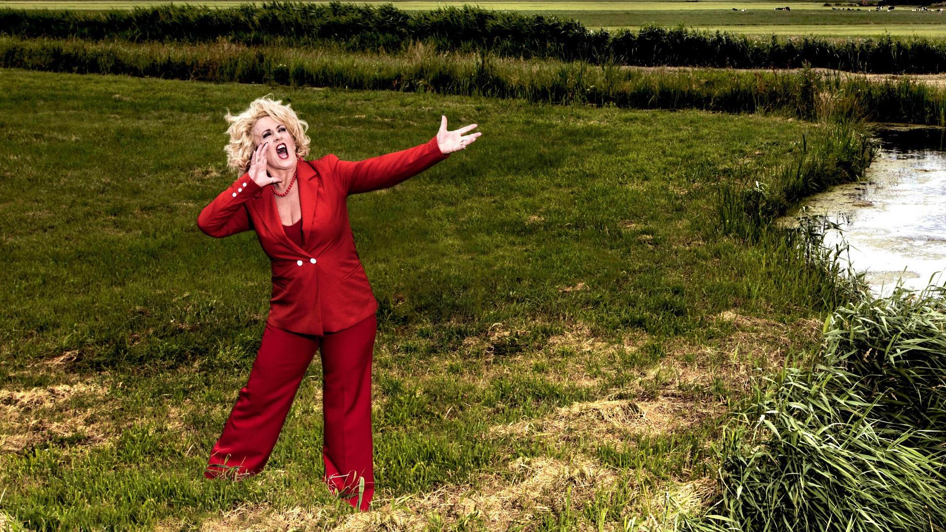 Karin Bloemen en band, Promotiefoto van Karin Bloemen in rood pak aan de oever van een riviertje in het veld