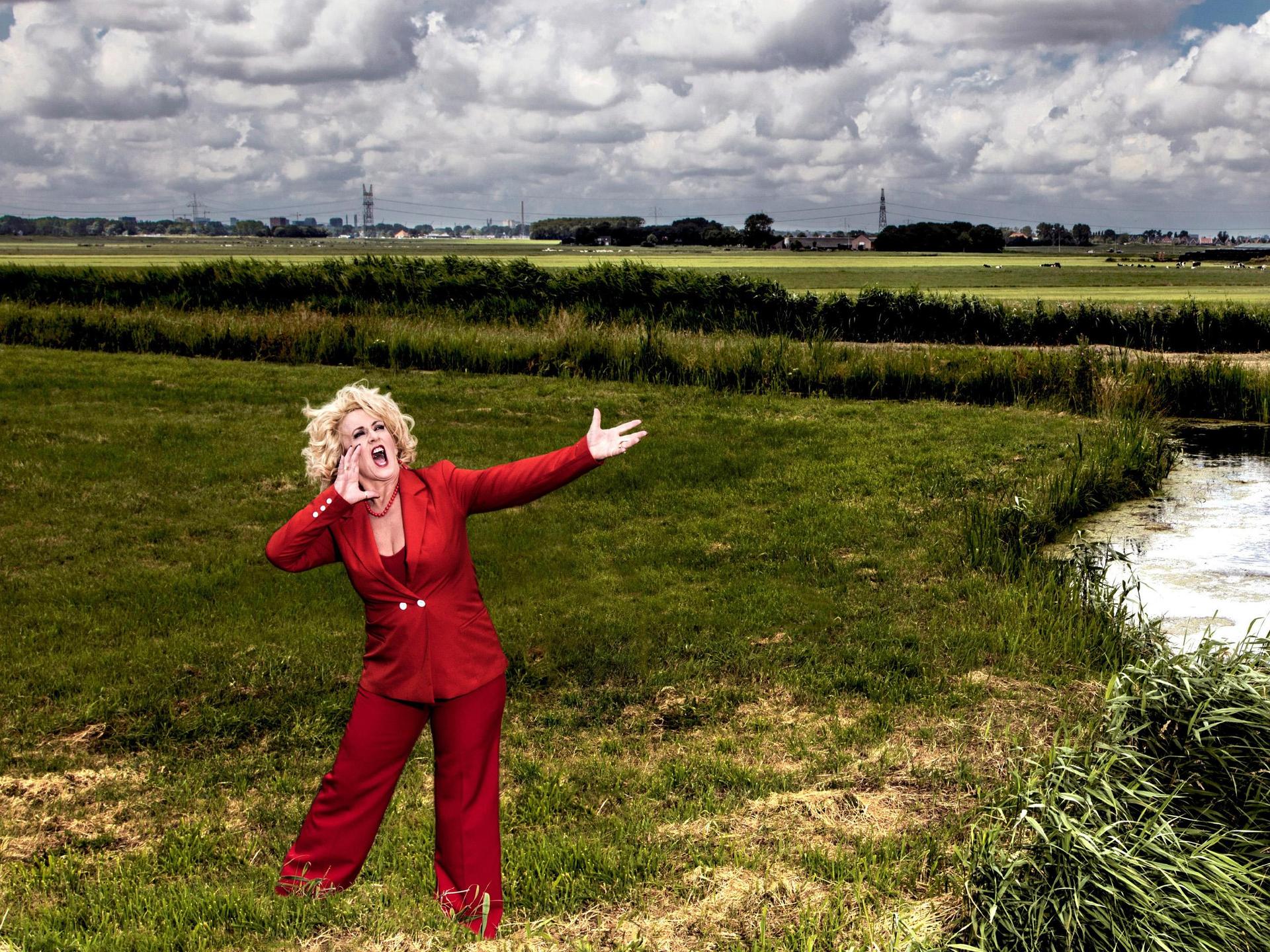 Karin Bloemen en band, Promotiefoto van Karin Bloemen in rood pak aan de oever van een riviertje in het veld