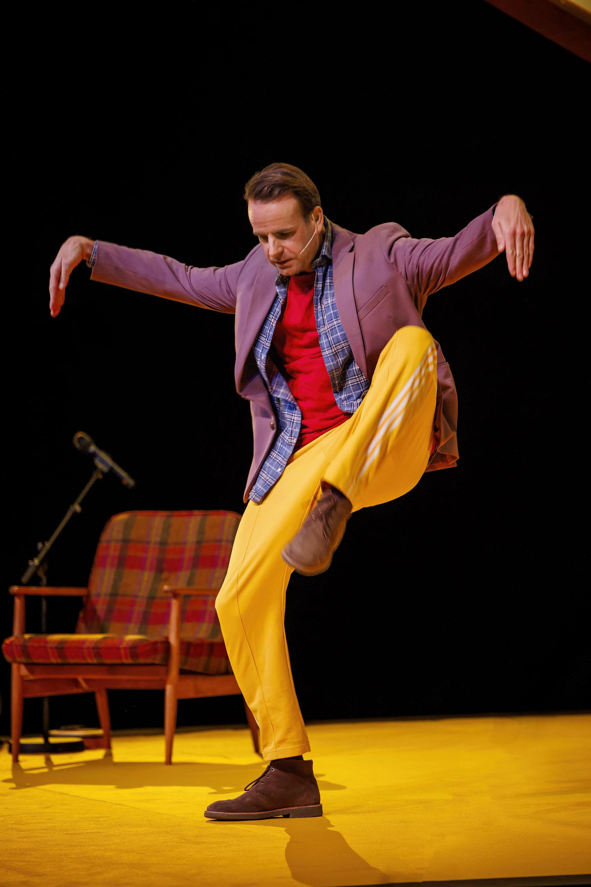 Scenefoto's van Henry van Loon op het podium met gele broek, rood shirt en jasje