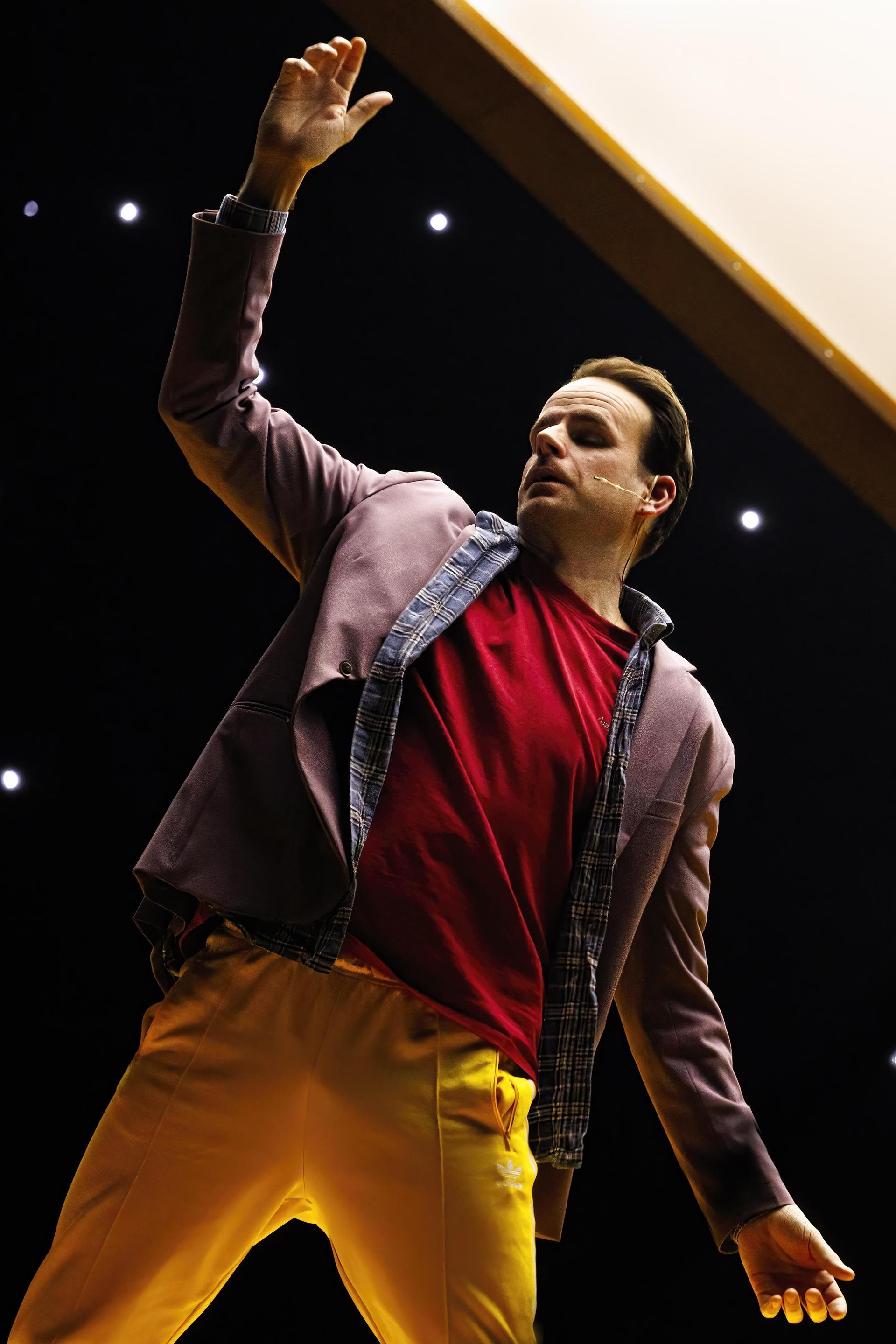 Scenefoto's van Henry van Loon op het podium met gele broek, rood shirt en jasje