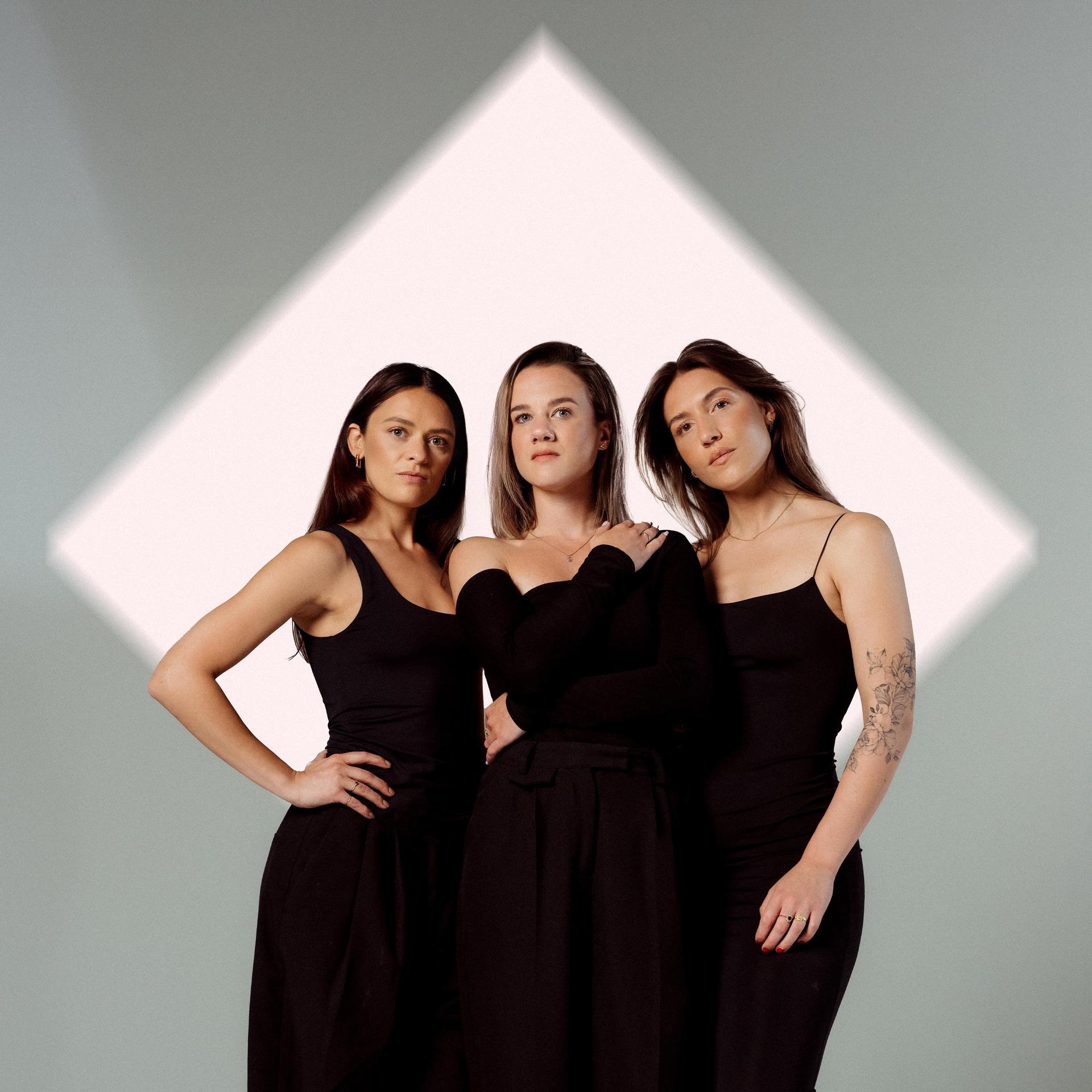 Velvet Vox, Promotiefoto van Velvet Vox - 3 achtergrond zangeressen in het zwart tegen een wit lichtblok