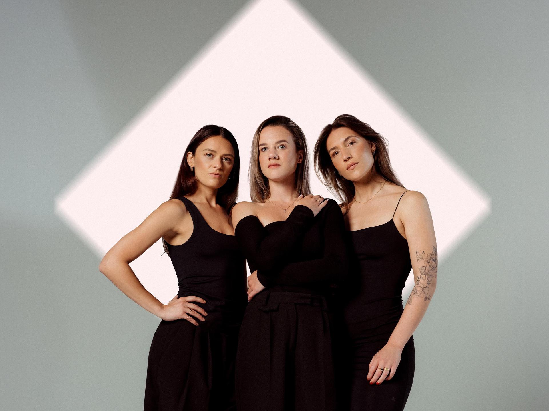 Velvet Vox, Promotiefoto van Velvet Vox - 3 achtergrond zangeressen in het zwart tegen een wit lichtblok