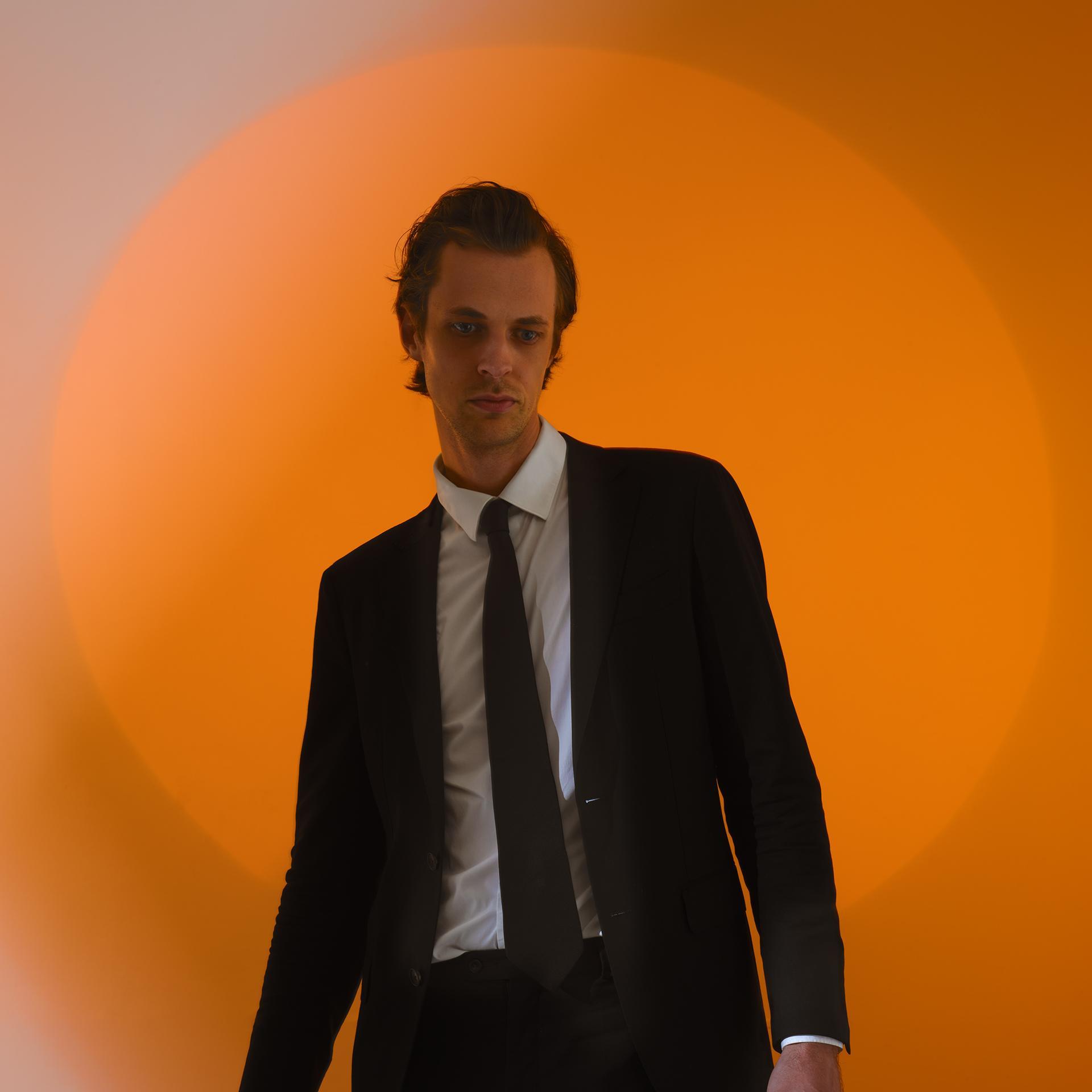 David Linszen, Promotiefoto van David Linszen in pak tegen een achtergrond met een oranje cirkel die vervaagd