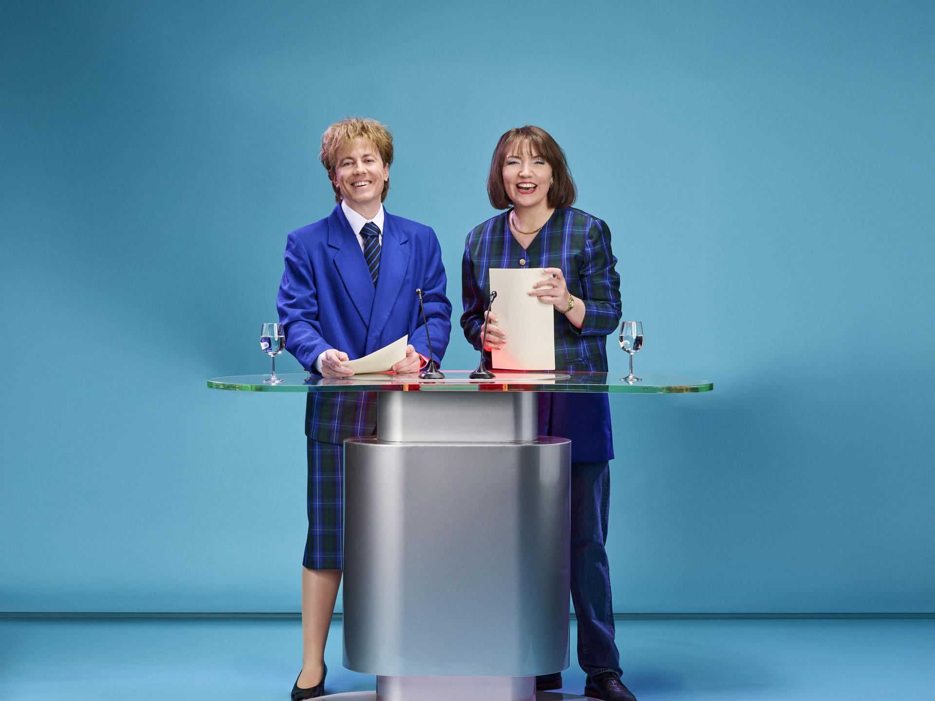 Blauwe Vinkjes, Promotiefoto van cabaretduo Blauwe Vinkjes achter een presentatiedesk