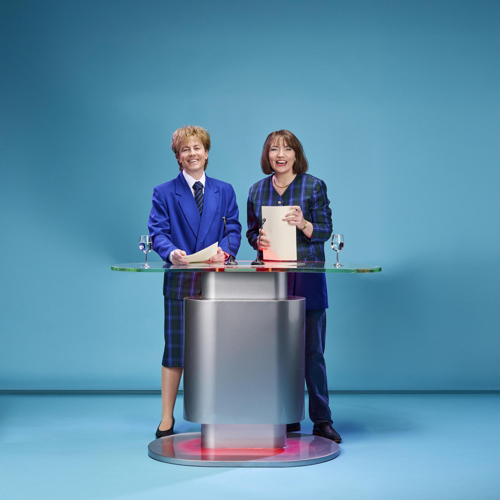 Blauwe Vinkjes, Promotiefoto van cabaretduo Blauwe Vinkjes achter een presentatiedesk