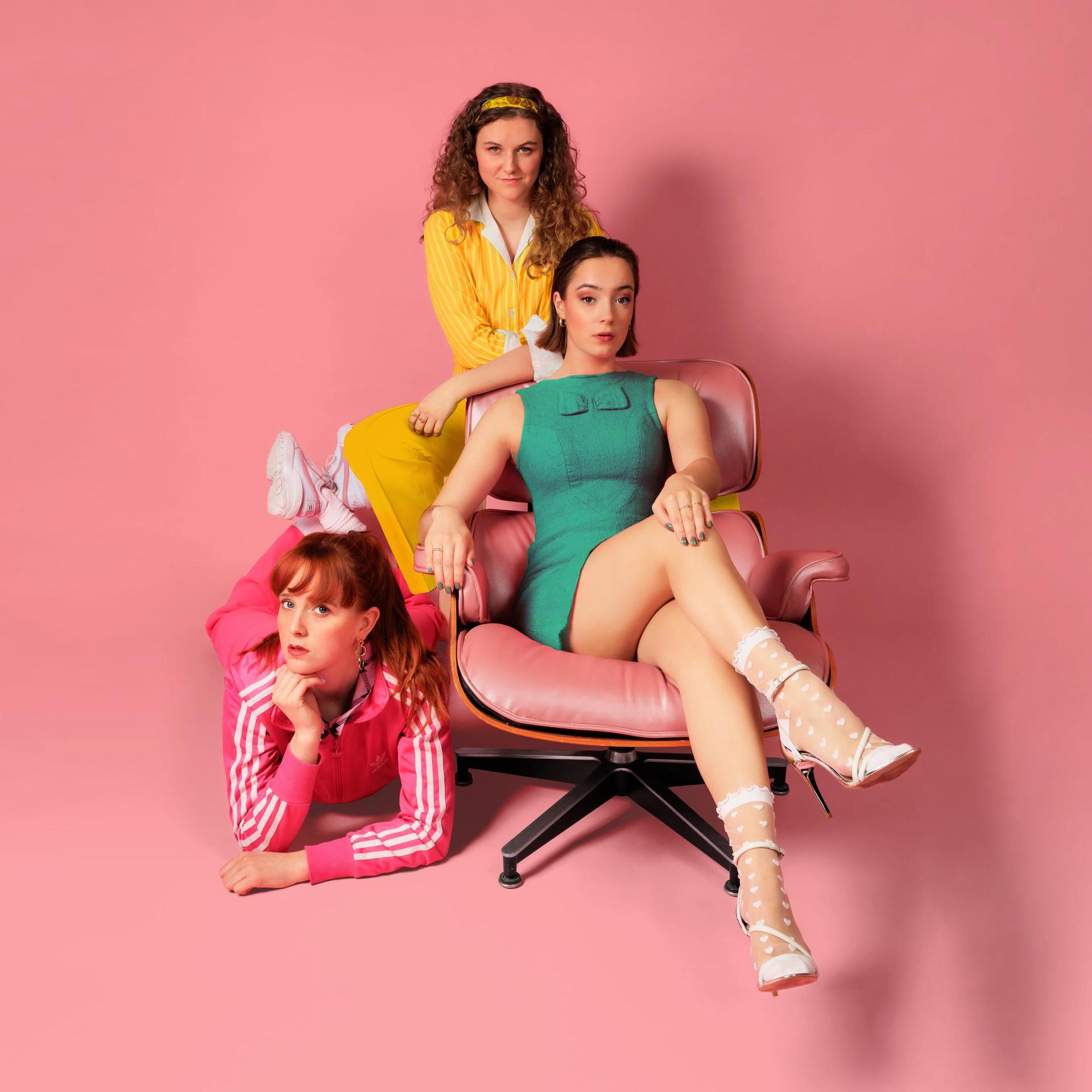 TRADWIVES de musical, Promotiefoto Tradwives met 3 dames in roze, geel en groen jurkje tegen roze achtergrond