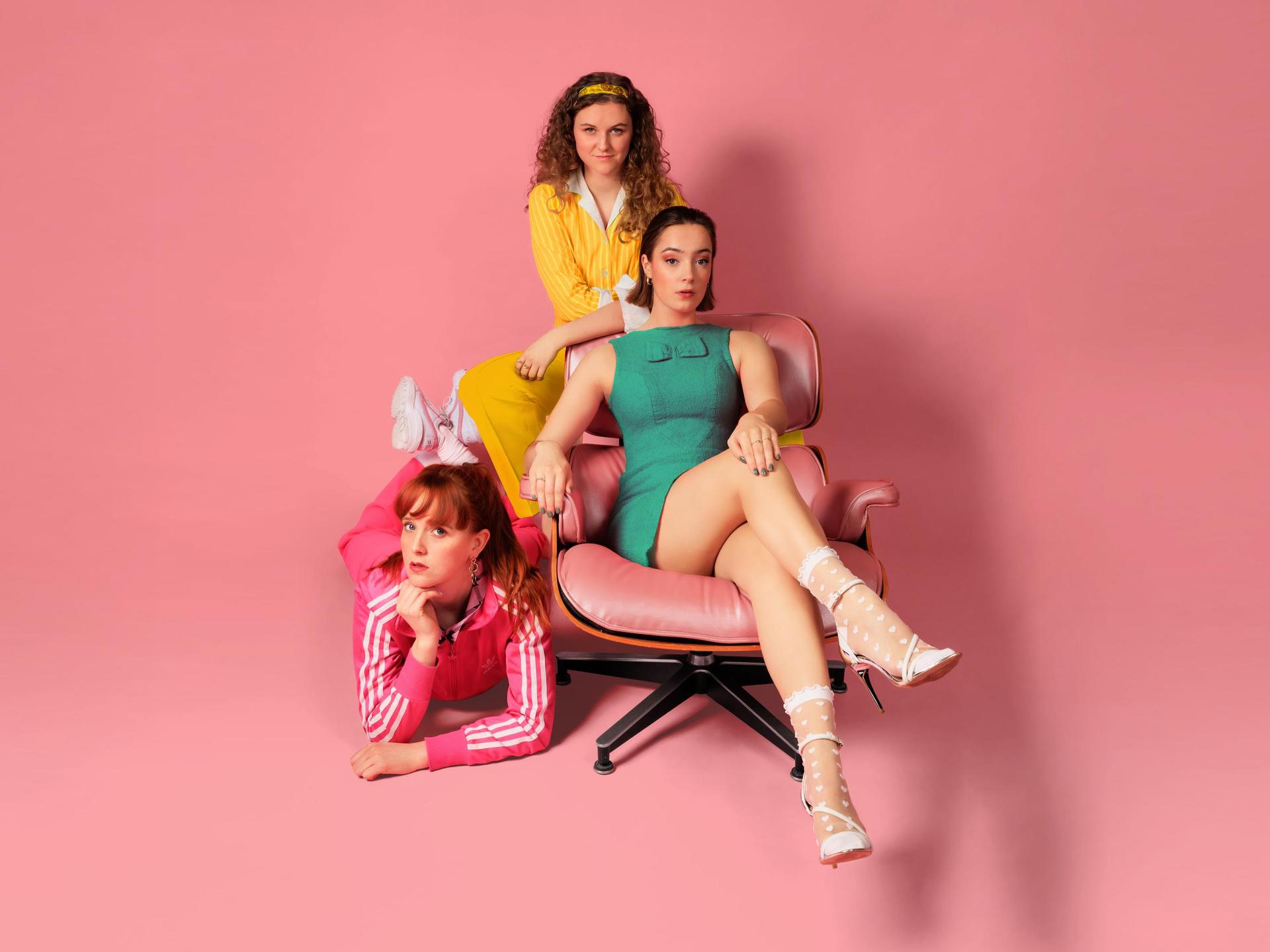 TRADWIVES de musical, Promotiefoto Tradwives met 3 dames in roze, geel en groen jurkje tegen roze achtergrond