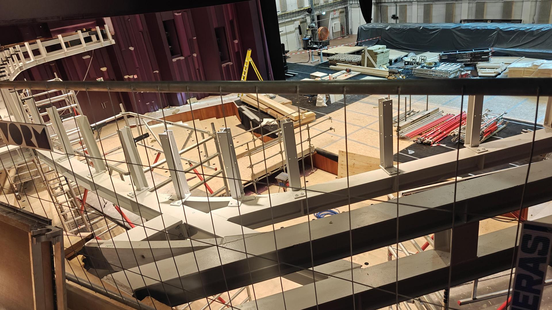 Grote zaal gezien vanaf de zijkant balkon richting podium ivm de stalen balken van het balkon