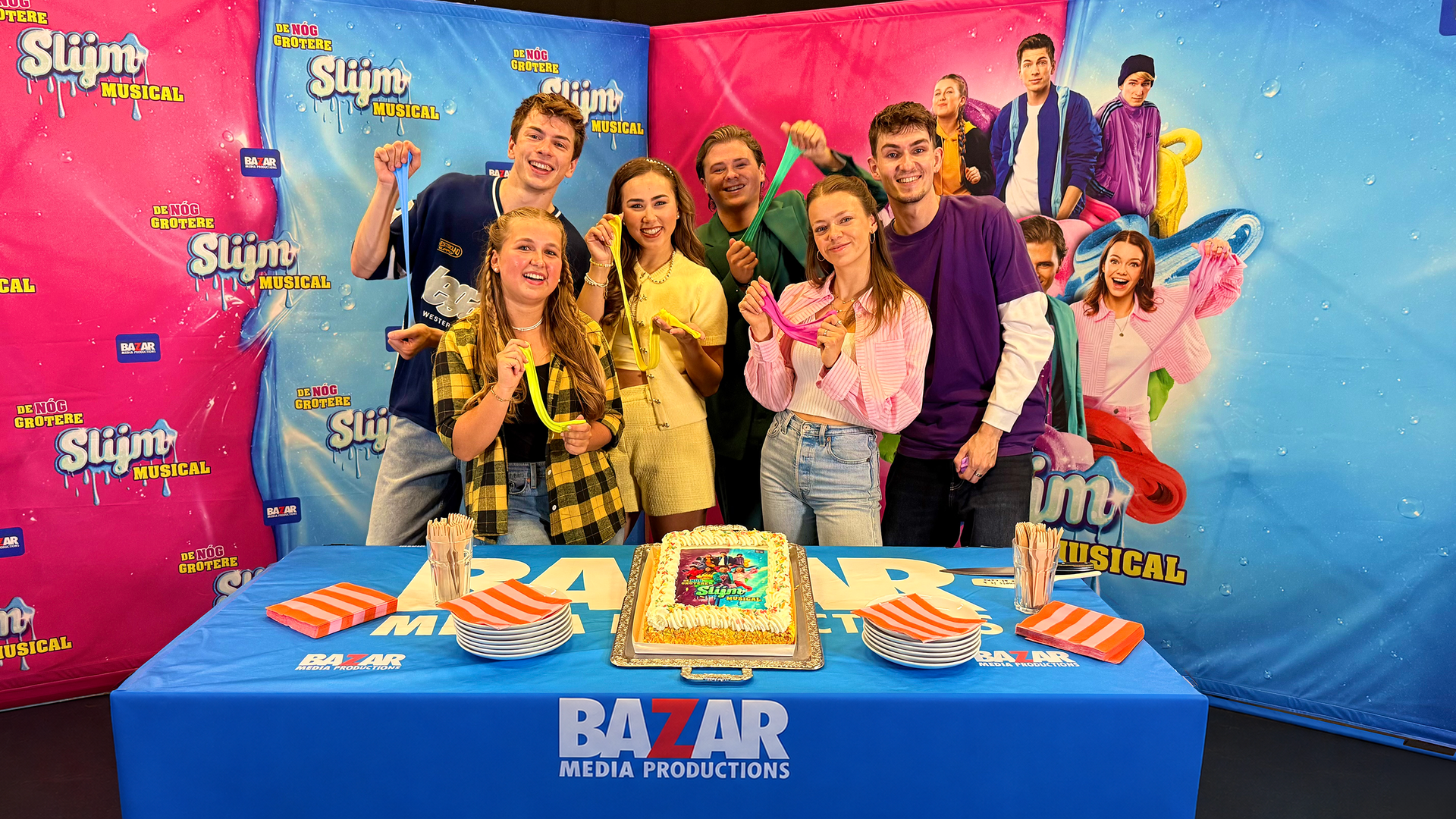 Foto van het taartsnijmoment met de cast van De Nog Grotere Slijmmusical van Bazar Media