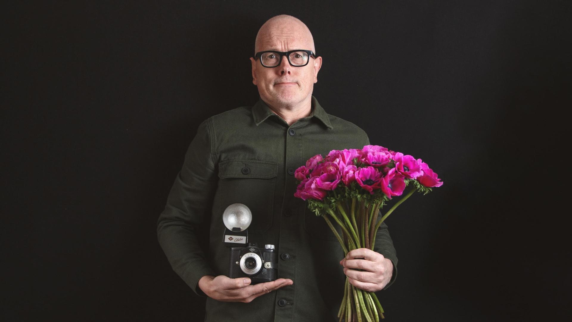 Kees van Amstel, Foto Kees van Amstel met in zijn ene hand een camera en in de andere roze bloemen