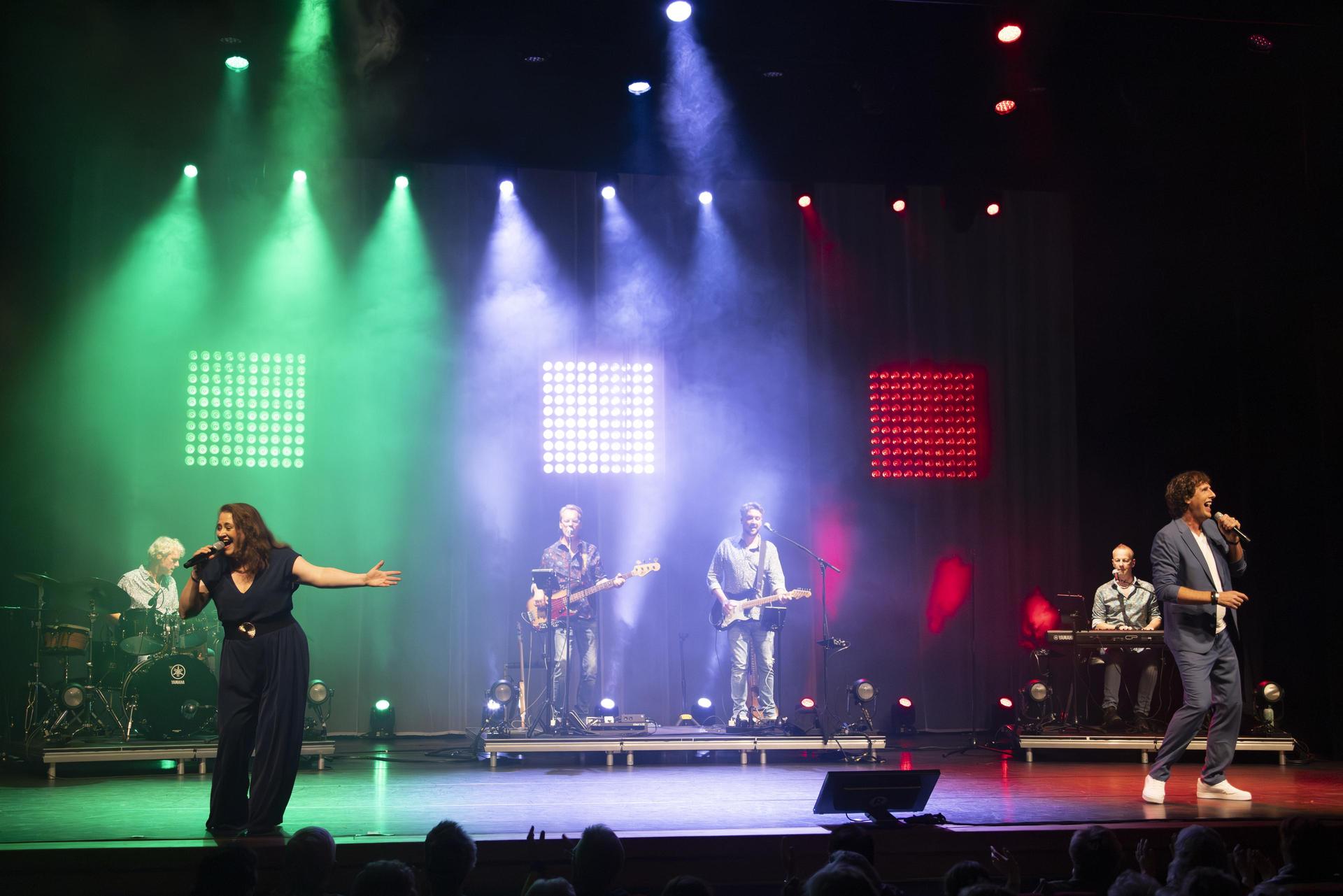 scènefoto van The Story of BZN met hele band op het podium met groen, blauw en rood licht belicht