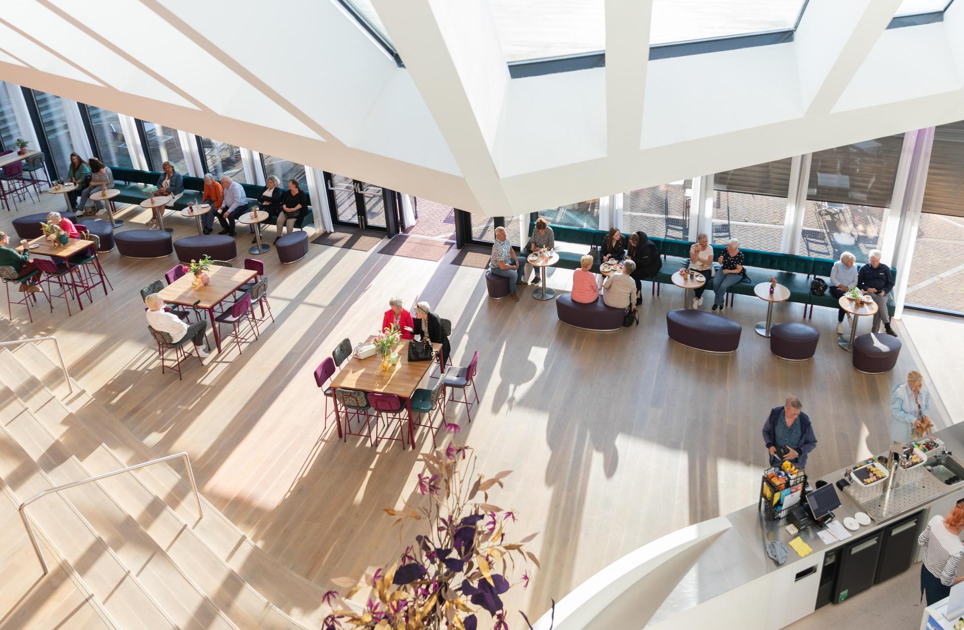 Foto van de foyer van Theater de Stoep met bezoekers bij daglicht genomen vanaf de bovenfoyer