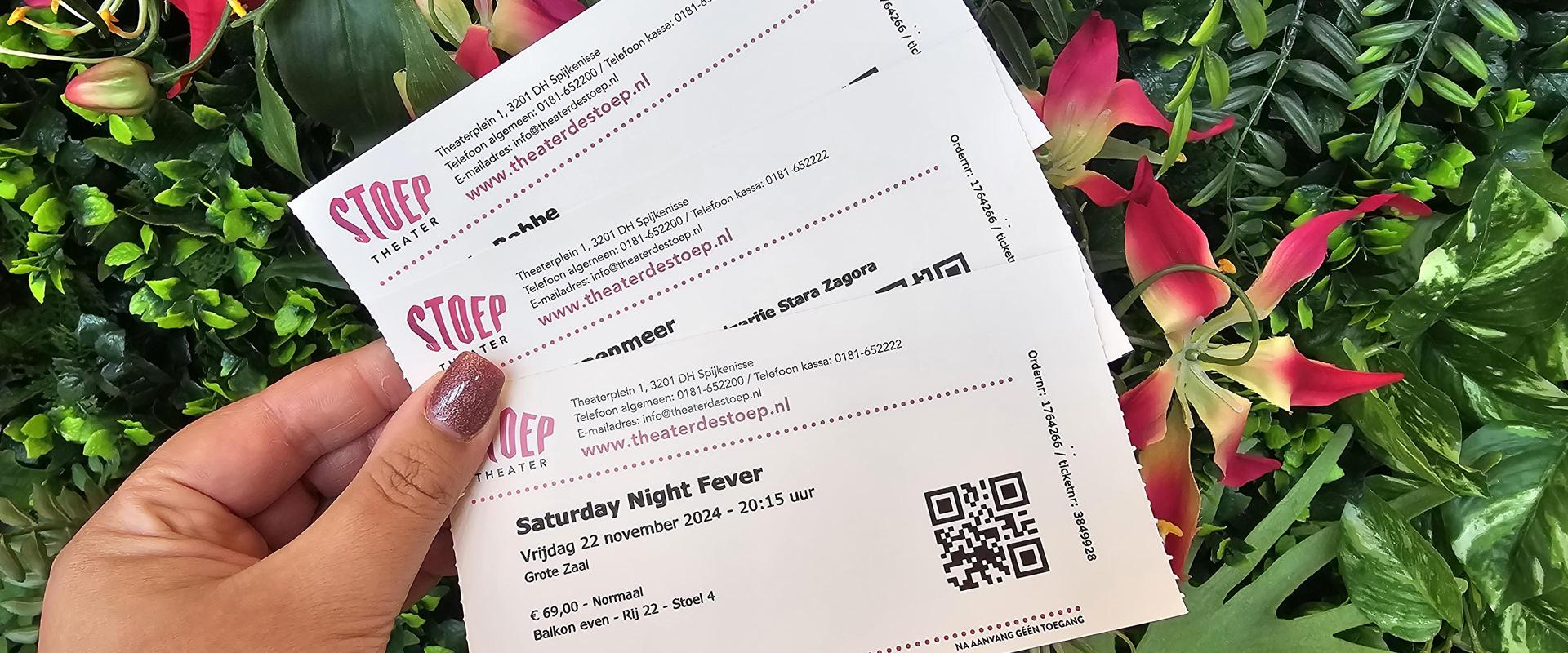 Foto van enkele tickets van Theater de Stoep in een hand vastgehouden tegen groene plantenachterwand