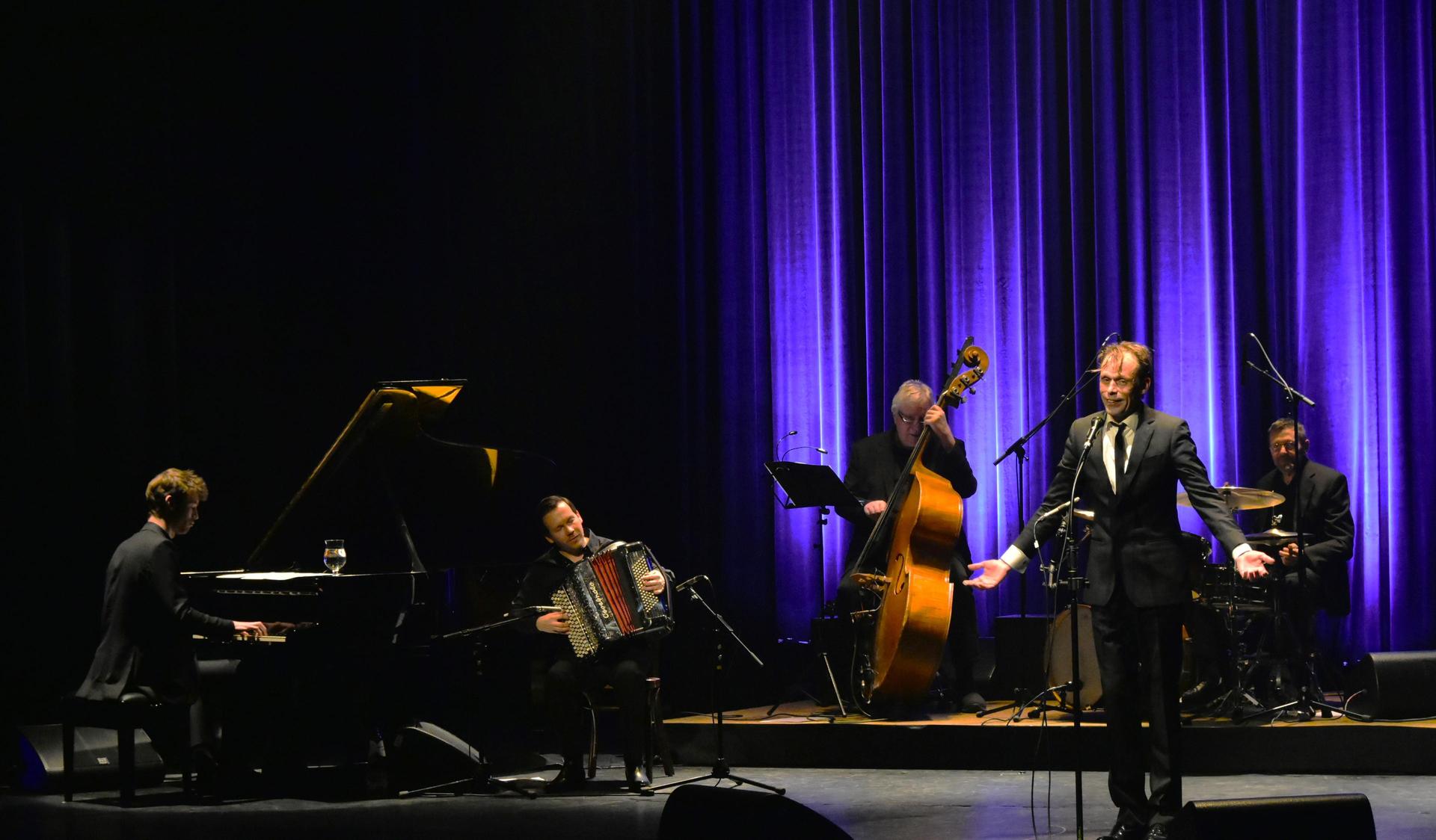 scènefoto van Filip Jordens op het podium zingend met muzikanten erachter
