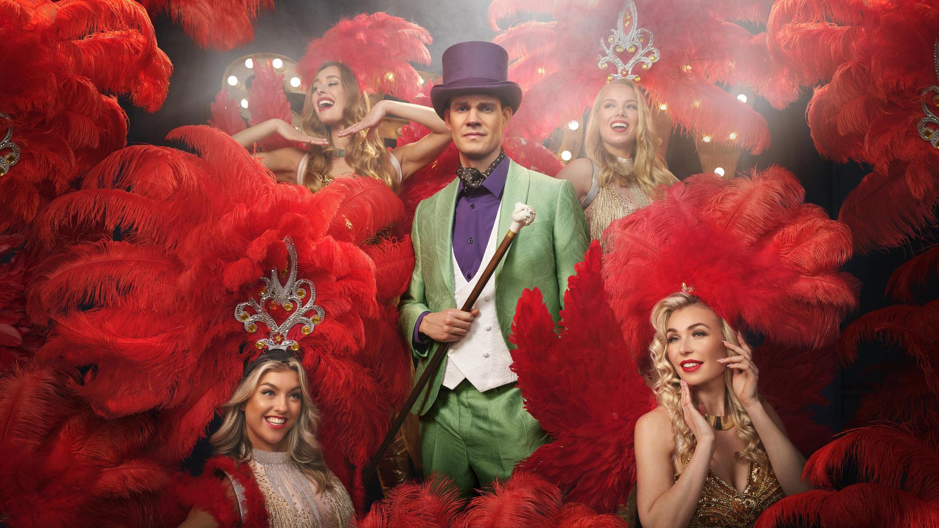 Tim Fransen, Foto van Tim Fransen in groen pak met paarse hoge hoed tussen de danseressen in roze grote jurken