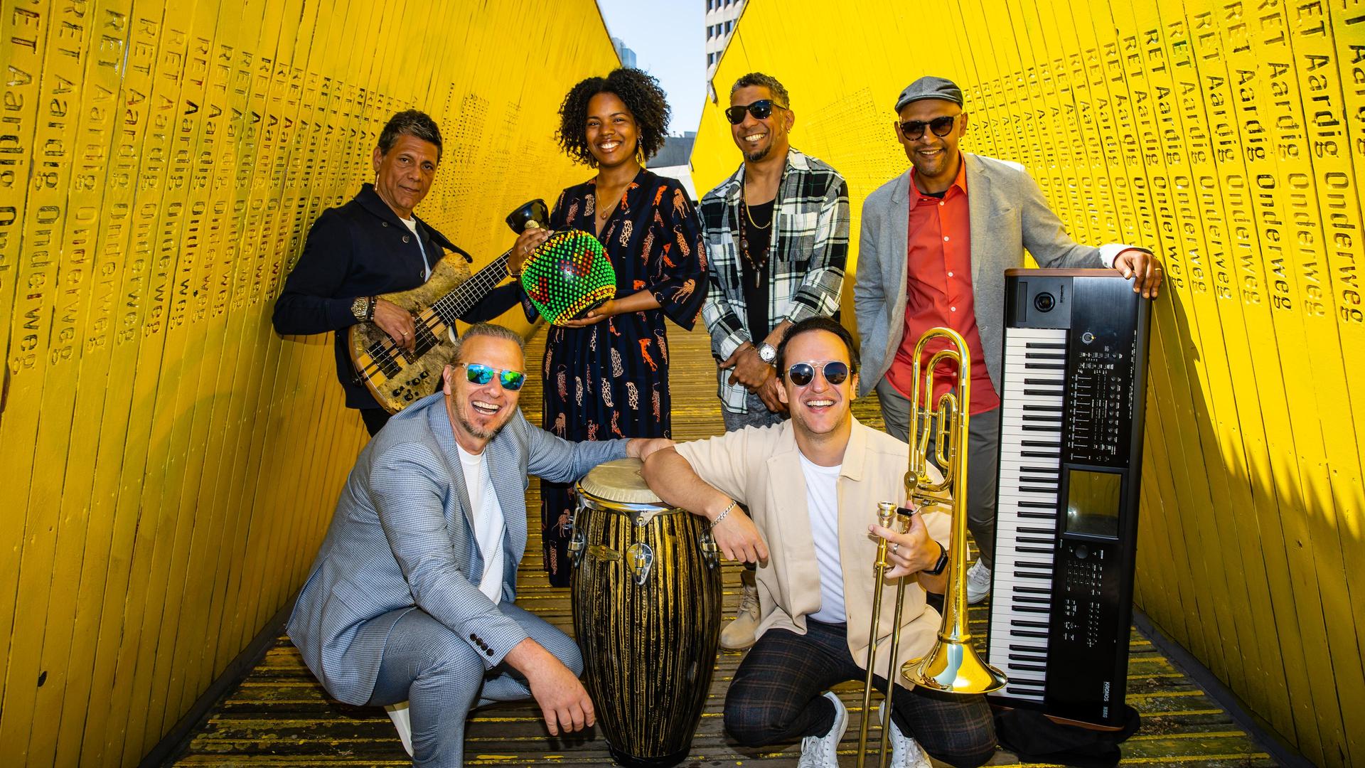 Stoep Jazz Presenteert: CaboCubaJazz, Foto van de band CaboCubaJazz met hun instrumenten tussen 2 gele muren