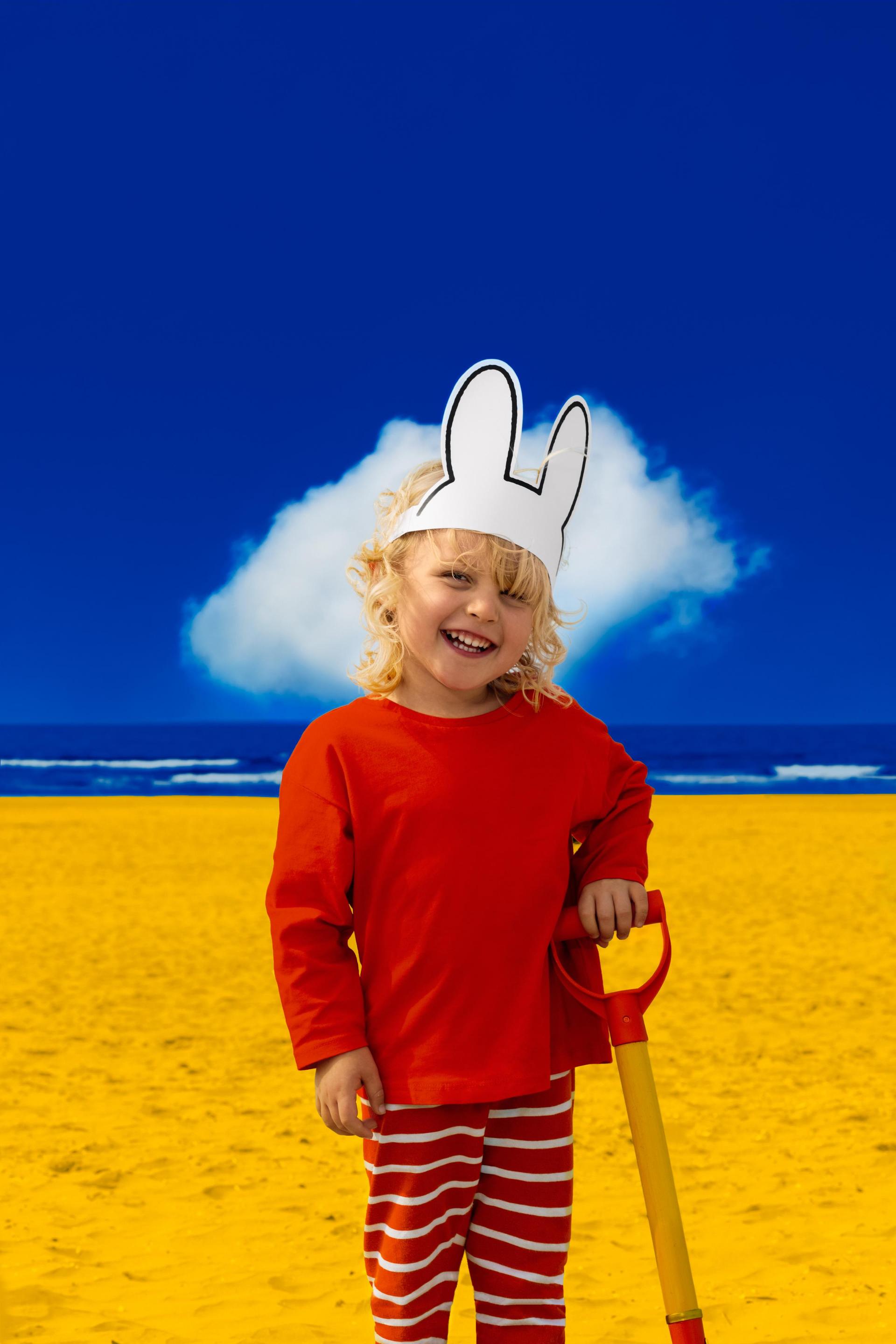 Foto van meisje op het strand met nijntje oren op en die een schep vasthoudt