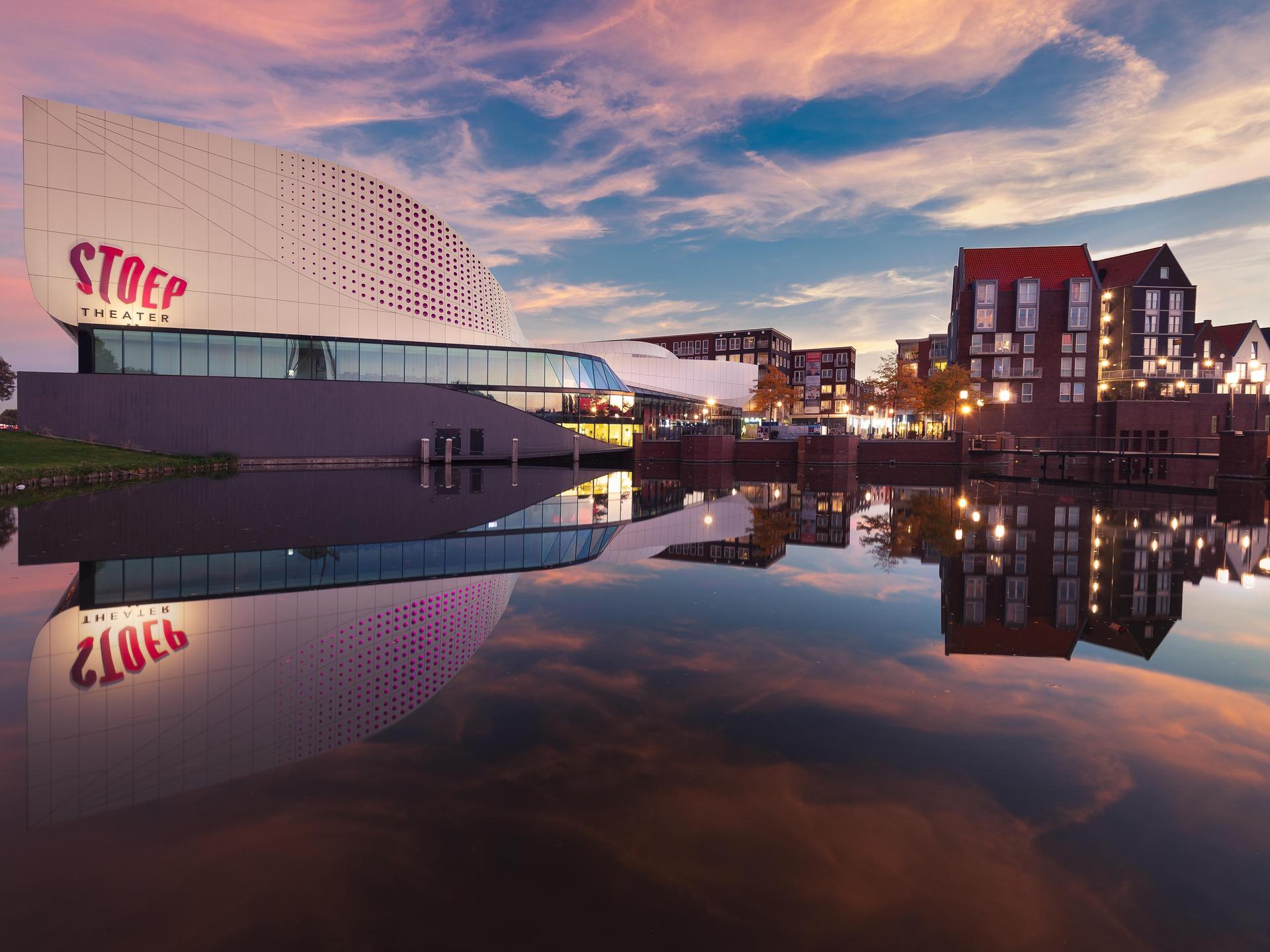 Foto van Theater de Stoep vanaf Schenkelweg genomen met mooie lucht en spiegeling in de vijver