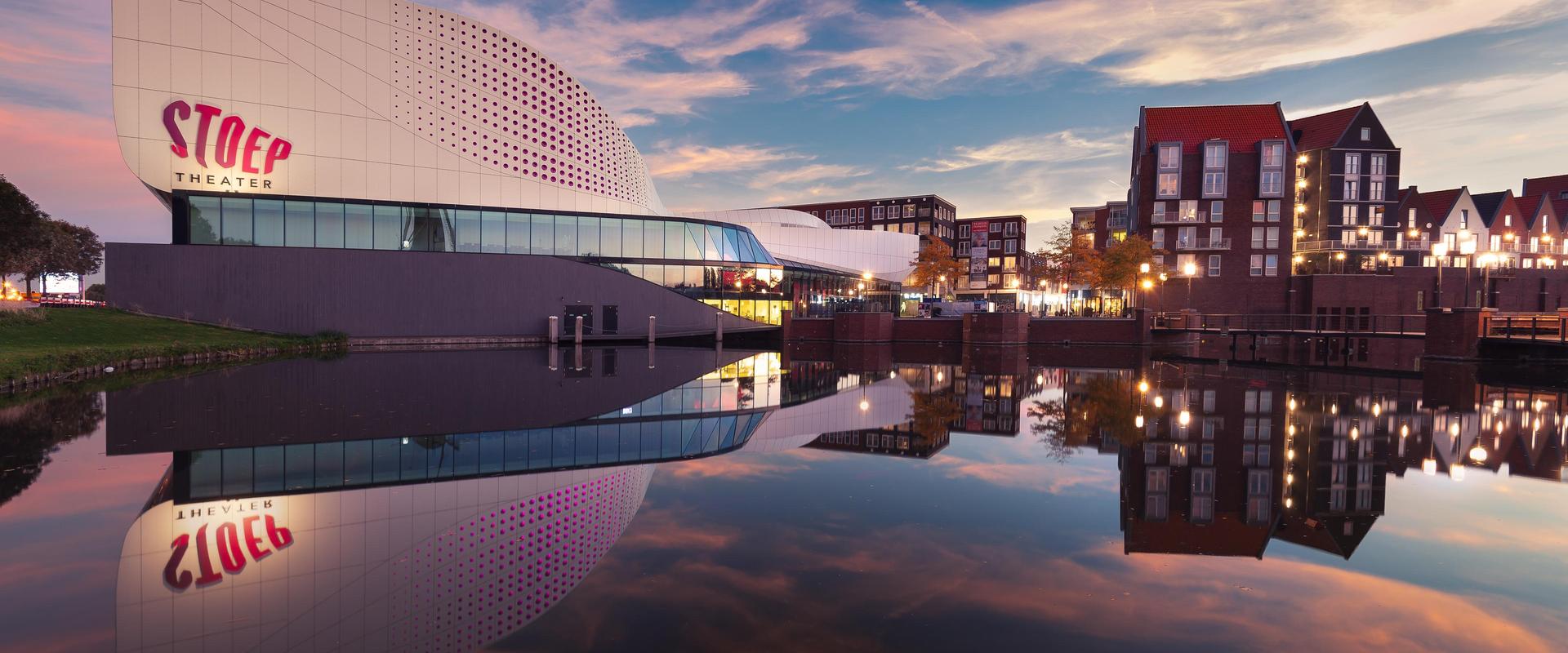 Foto van Theater de Stoep vanaf Schenkelweg genomen met mooie lucht en spiegeling in de vijver