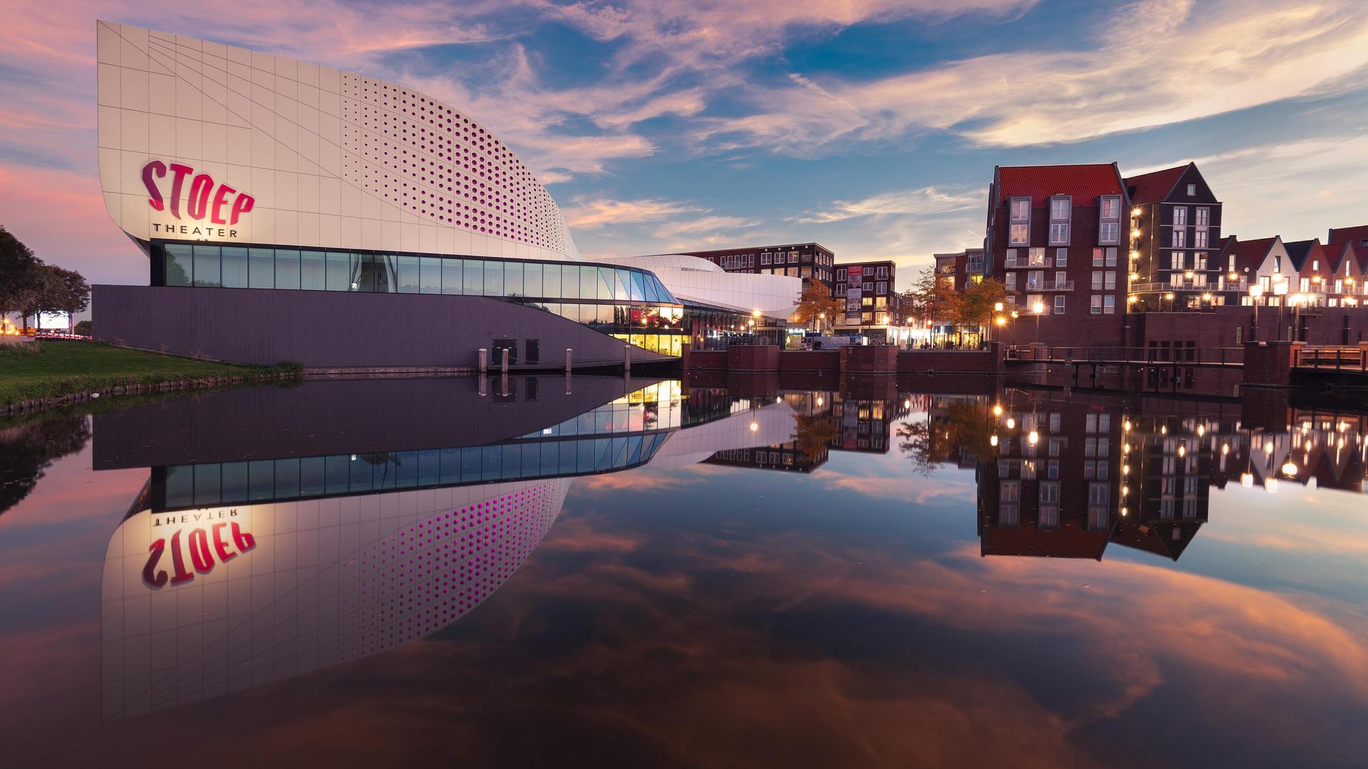 Foto van Theater de Stoep vanaf Schenkelweg genomen met mooie lucht en spiegeling in de vijver