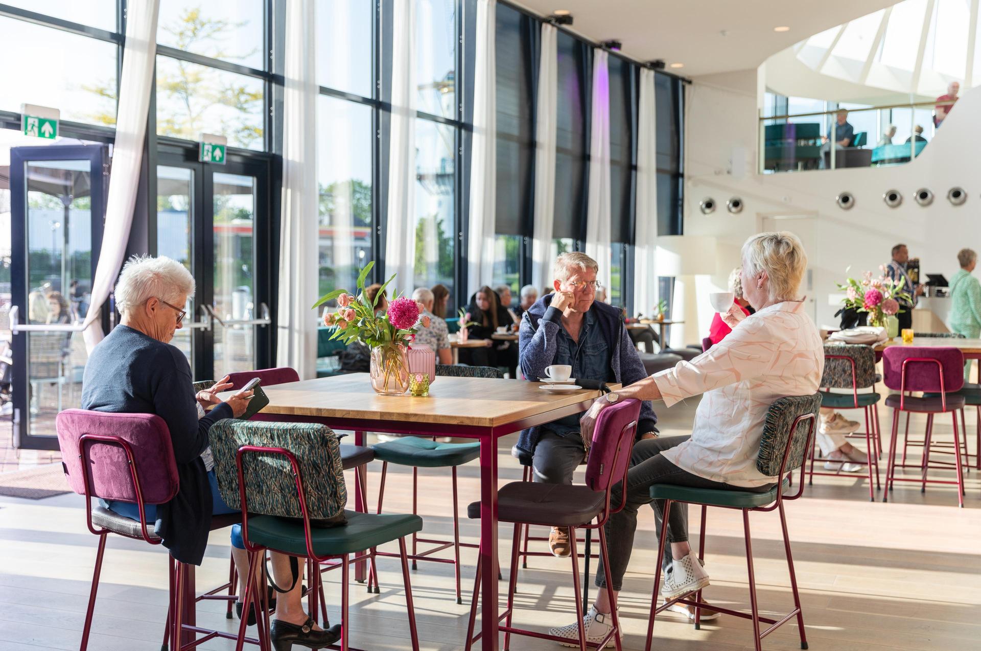 Foto van 3 bezoekers aan een tafel in het theatercafé van Theater de Stoep bij daglicht