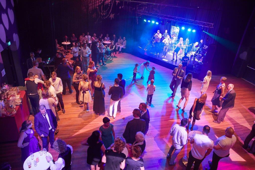 Foto van mensen in de Kleine Zaal met ingeklapte tribune en band in de hoek van de zaal