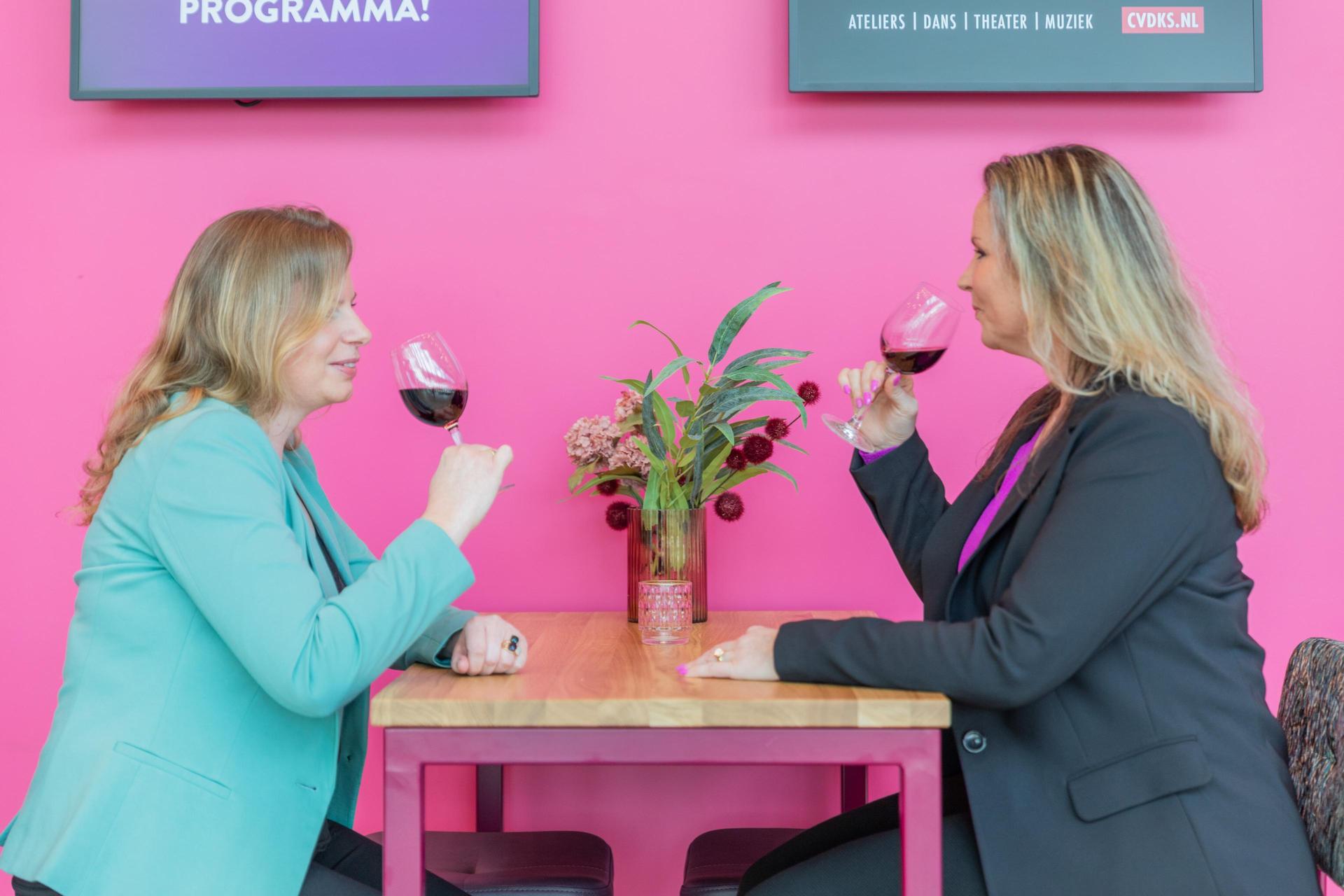 Foto van 2 vrouwen aan een tafeltje in de foyer van Theater de Stoep die samen wijn drinken